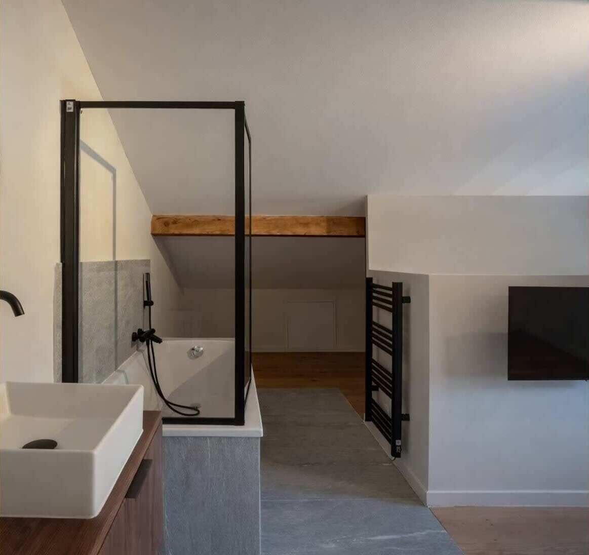 Une salle de bain moderne avec une baignoire sur pieds, un grand miroir et une poutre en bois au plafond.