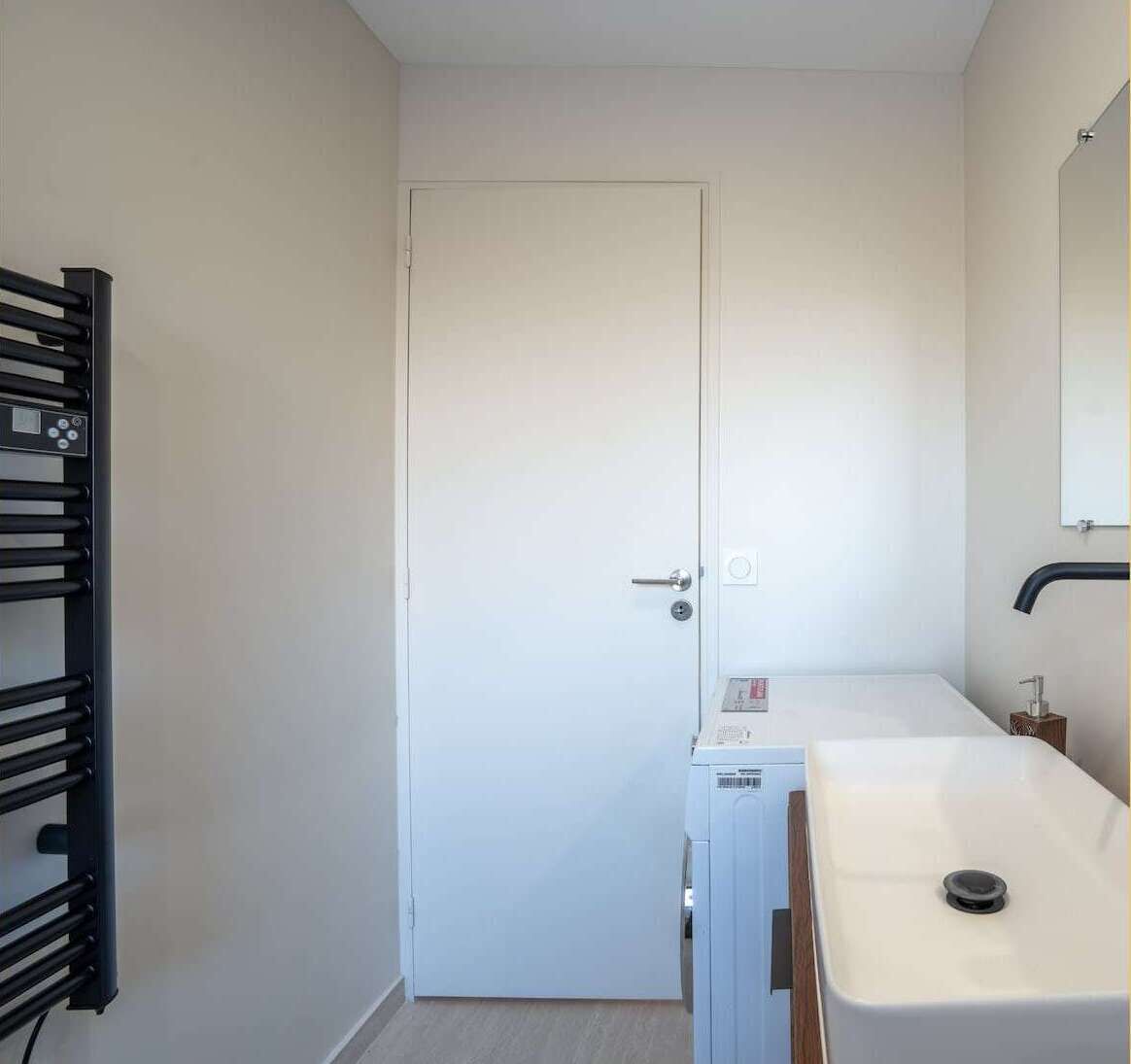 A small, clean room with a white door, a white sink, and a black towel rack.