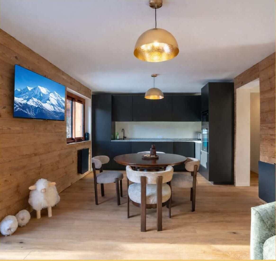 Ett modernt matområde med ett runt bord och stolar, en stor hänglampa och en tavla med ett bergsmotiv på väggen.