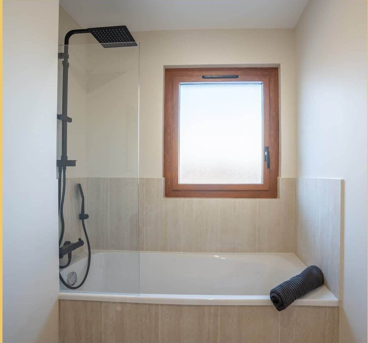 A bathroom with a bathtub, a showerhead, and a window.