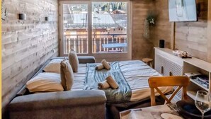 Een kamer met een bed, een bureau, een stoel, een televisie en een raam met uitzicht op gebouwen.