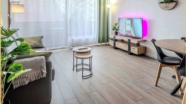 Moderni olohuone, jossa on sohva, sohvapöytä, televisio sekä ruokailutila pöytineen ja tuoleineen.