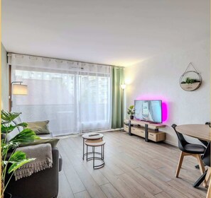 Ein modernes Wohnzimmer mit einer Couch, einem Couchtisch, einem Fernseher und einem Essbereich mit Tisch und Stühlen.
