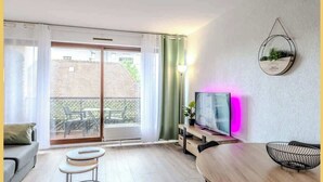 Moderni olohuone, jossa on puinen ruokapöytä, jalustalla oleva televisio ja parveke, jolta on näkymä naapurustoon.