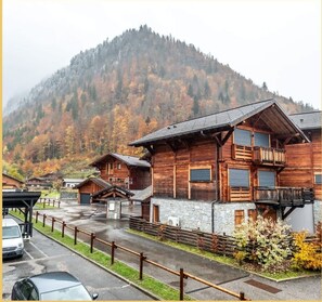 A wooden cabin with a stone foundation, a balcony, and a view of a forested mountain. - Le Soleil Blanc I T2 I Montriond (Montriond)