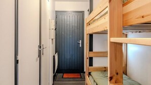 Un couloir étroit, avec des lits superposés d’un côté et une porte au fond.