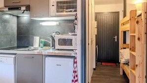 Une cuisine compacte équipée d’un four à micro-ondes, d’un lave-vaisselle et d’un évier. Un lit superposé en bois se trouve sur la droite.