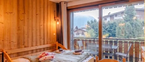 A wooden room with a bed, a table, and a view of houses and trees.