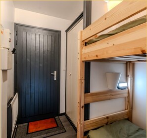 A compact room with a dark wooden door, a bunk bed, a small bedside table, and a red doormat. - Le Paradisio I Studio I Morzine (Morzine)