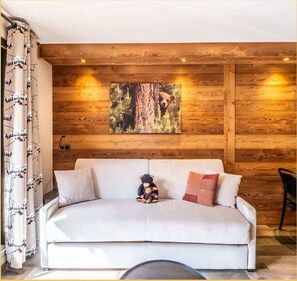 Ein gemütliches Zimmer mit einem weißen Sofa, einem Kuschelbären und einem Waldbild an der Holzwand.