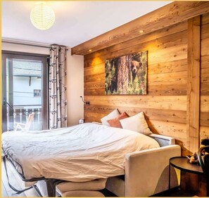 Ein Schlafzimmer mit einem großen Bett, einer Holzwandverkleidung, einem Gemälde und einem Balkon mit Blick.