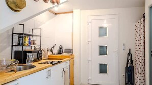 A compact kitchen with a wooden countertop, a sink, and a built-in oven. There is a black metal shelf with kitchen items and a white door with frosted glass panels. - L'Etable de Larringes (Larringes)