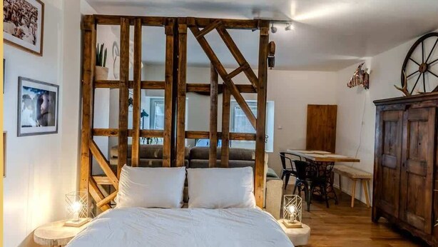 A bedroom with a large bed, wooden beams, a wooden cabinet, and a dining area. - L'Etable de Larringes (Larringes)