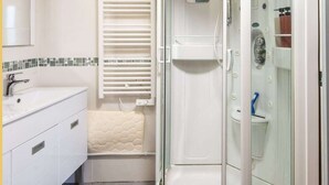 A modern bathroom with a white vanity, a glass-enclosed shower, and a built-in toilet. - L'Etable de Larringes (Larringes)