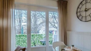 Ein Zimmer mit großem Fenster, einer Couch, einem Glastisch mit Stühlen und einer Wanduhr.