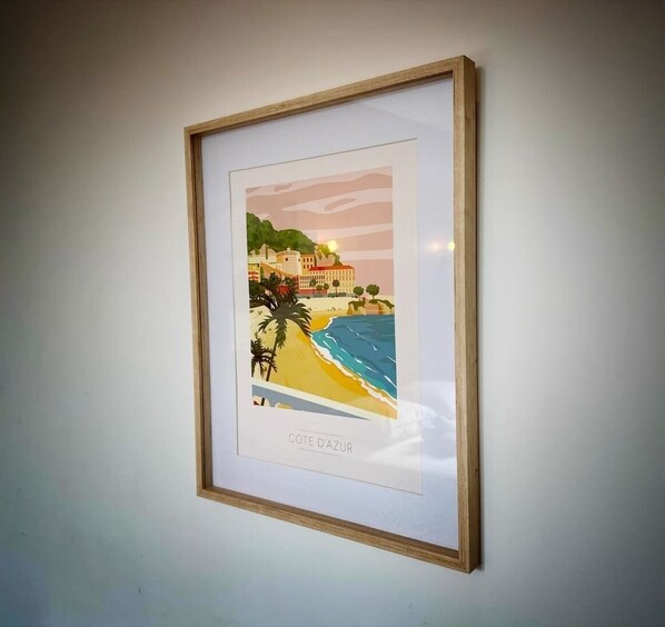 A framed artwork depicting a beach scene with a building and palm trees.