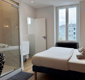 A bedroom with a bed, a window with a view, a door, and a bathroom with a mirror and sink.