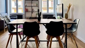 En moderne stue med et træspisebord, sorte stole, en reol og et stort vindue med udsigt til bygninger.