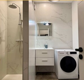 Un baño moderno con ducha, lavabo, espejo y lavadora.
