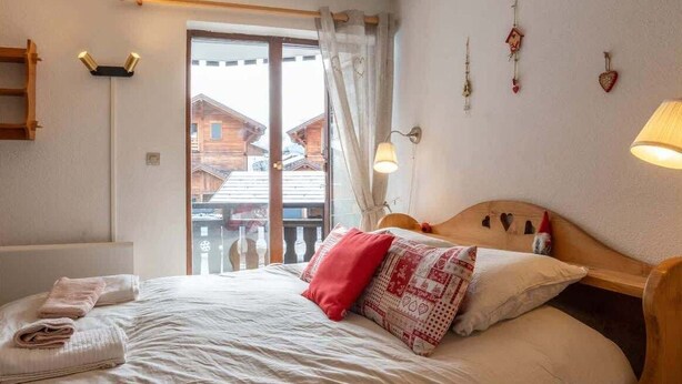 Ein gemütliches Schlafzimmer mit einem Holzbett, einem Fenster mit Vorhängen und Blick auf Gebäude.