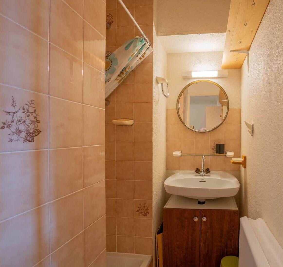 A bathroom with beige tiles, a wooden cabinet, a white sink, and a mirror.