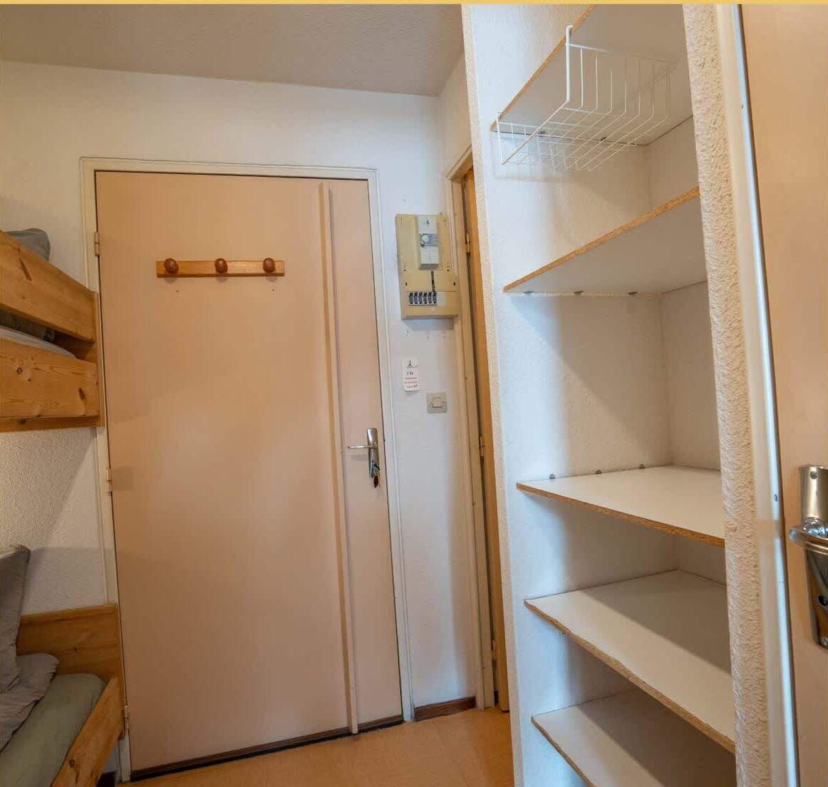 A room with a door, a small electrical panel, and a shelving unit.