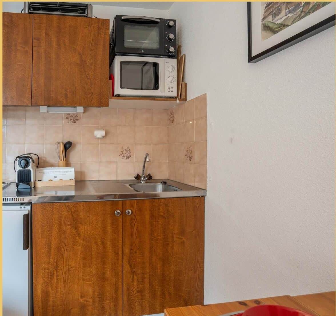 Una cocina compacta con armarios de madera, un microondas, un tostador y un lavamanos.