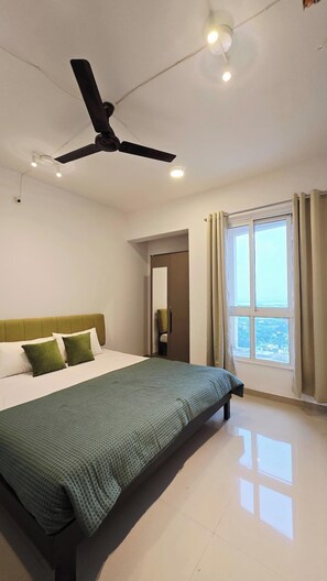 Une chambre d’hôtel moderne, équipée d’un lit, d’un ventilateur de plafond, d’une fenêtre avec des rideaux et offrant une vue sur le paysage urbain.