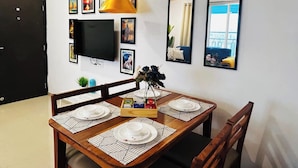 A dining area with a wooden table set for four, a TV mounted on the wall, and framed pictures on the wall.