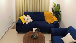 A modern living room with a blue sofa set, a round coffee table with a vase of flowers, and a black chandelier.