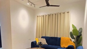 A modern living room with a blue sofa, a round coffee table, a small side table, a ceiling fan, and a chandelier.