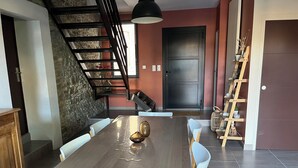 Uma sala de jantar com uma mesa e cadeiras de madeira, uma parede de pedra, uma escada e uma porta.