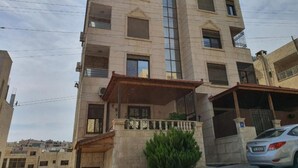 A multi-story building with a central vertical glass facade, balconies, and a car parked in front. - Shahed Apartment 3-bedroom apartment in charming Amman with comfort (Amman)