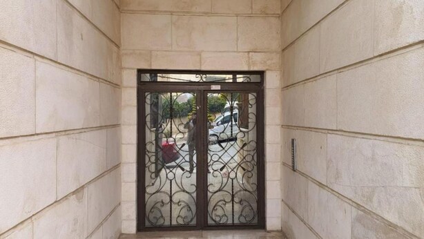 A corridor with a double door featuring decorative metalwork, leading to an outdoor area with parked cars and a visible street. - Shahed Apartment 3-bedroom apartment in charming Amman with comfort (Amman)