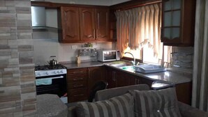 A compact kitchen with a gas stove, oven, microwave, and a small dining area with a sofa. - Shahed Apartment 3-bedroom apartment in charming Amman with comfort (Amman)