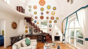 A spacious living room with a high ceiling, a fireplace, and a staircase leading to an upper level.