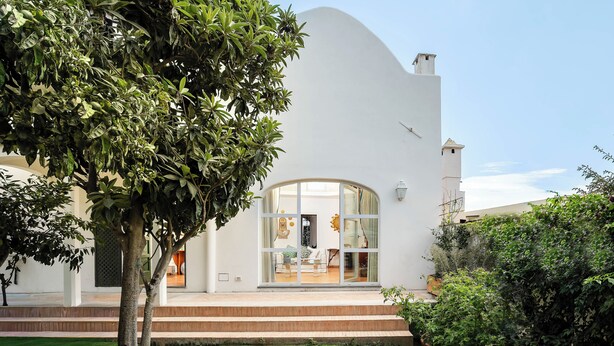 A modern house with a white exterior, a glass door entrance, and a well-maintained lawn.