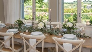 A dining table set for six with white plates, glasses, and a centerpiece of flowers and greenery.