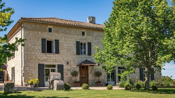 A stone building with a tiled roof, a central entrance, and a well-maintained lawn.