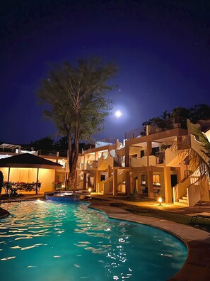 A nighttime view of a hotel with a swimming pool, a large tree, and a moon in the sky. - Tropical 2nd floor Condo with Rooftop (Playas Del Coco)