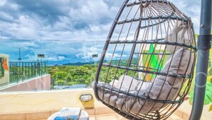 A hanging chair with cushions on a balcony with a view of greenery and a distant mountain range. - Casa Elevación | Ocean-View Rooftop Retreat | Pool | Fiber WiFi (Playas Del Coco)