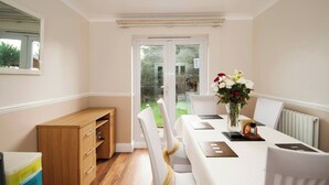 A dining area with a table set for two, white chairs, a vase with flowers, and a wooden cabinet. - Room-private Double Room Ensuite in Ches (Waltham Cross)