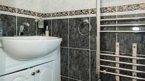 A bathroom with a white sink, a mirror, a towel rack, and a shower area with a tiled wall. - Room-private Double Room Ensuite in Ches (Waltham Cross)