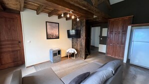A spacious living area with a sofa, a television mounted on a wooden wall, and a small table with a chair. - Soie - Fabulous 1-bedroom apartment in quaint Seillans (Seillans)