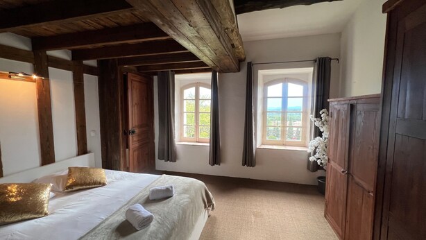 A bedroom with a bed, wooden wardrobe, two windows with curtains, and a view of greenery outside. - Soie - Fabulous 1-bedroom apartment in quaint Seillans (Seillans)