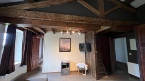 A room with exposed wooden beams, a television mounted on the wall, a small table with a towel, and a staircase leading to another level. - Soie - Fabulous 1-bedroom apartment in quaint Seillans (Seillans)