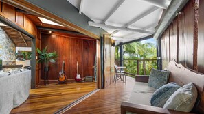 Une pièce spacieuse avec un plancher en bois, un canapé agrémenté de coussins à motifs, une guitare, un haut-parleur et une plante en pot.