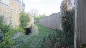 A narrow alleyway with a stone wall on one side and a wooden fence on the other, leading to a small entrance. - Village house with 2 bedrooms, garden and outdoor swimming pool (Distré)