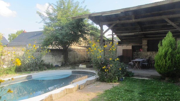 A swimming pool surrounded by a stone wall, a wooden deck, and a covered patio area. - Village house with 2 bedrooms, garden and outdoor swimming pool (Distré)