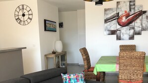Una sala moderna con un sofá oscuro, un cojín tejido colorido, una mesa de centro de madera, una silla de mimbre y arte abstracto en la pared.